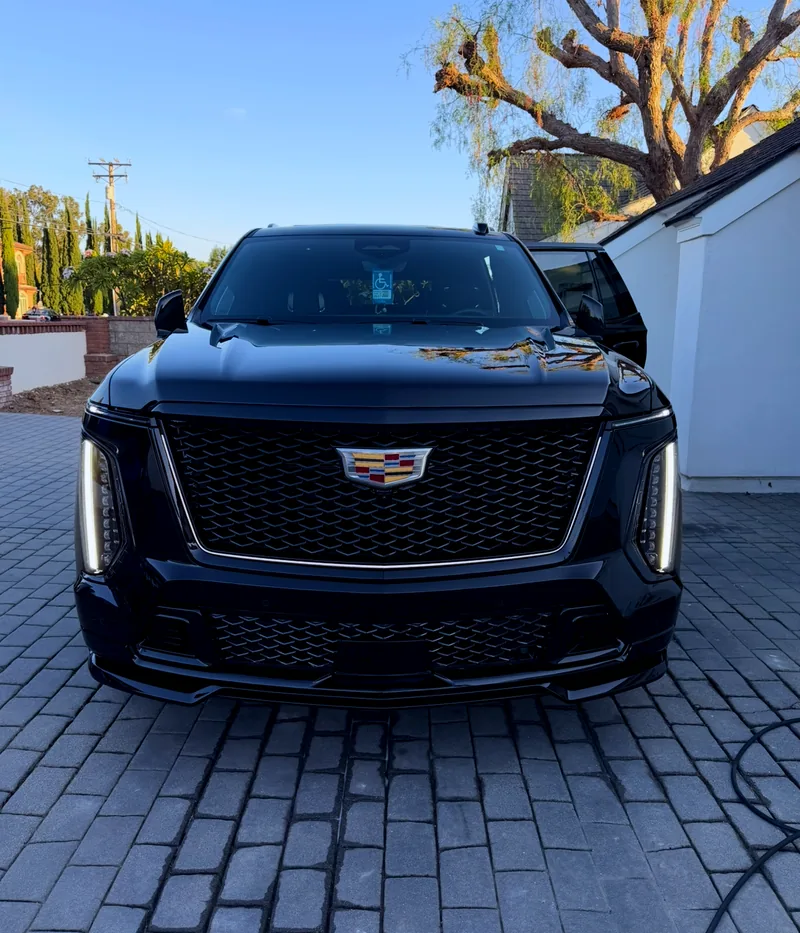 A black Escalade at golden hour on a paver driveway, a tree reflected cleanly in the hood.