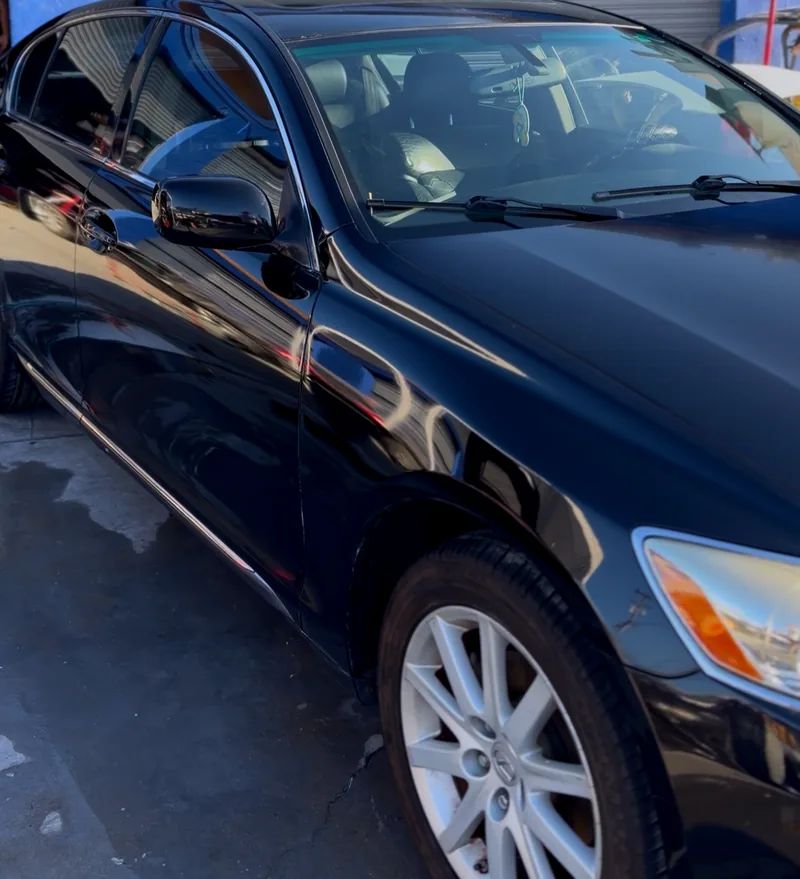 The flank of a black Lexus after a maintenance wash, the reflection running unbroken down the door.